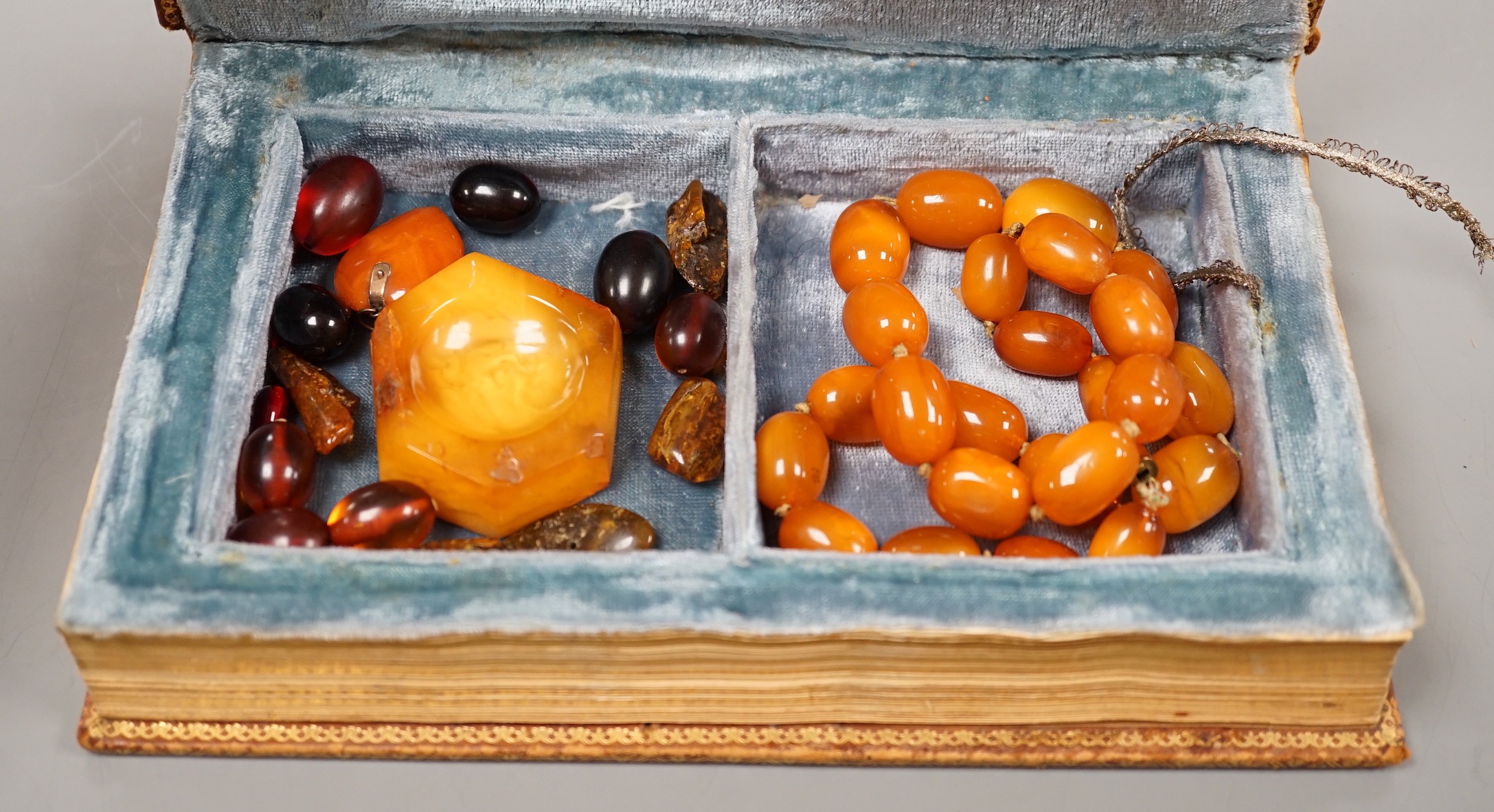 A single strand amber bead necklace, 48cm, gross 52 grams, together with other loose amber and amberoid beads and an amber pendant in a simulated book box.